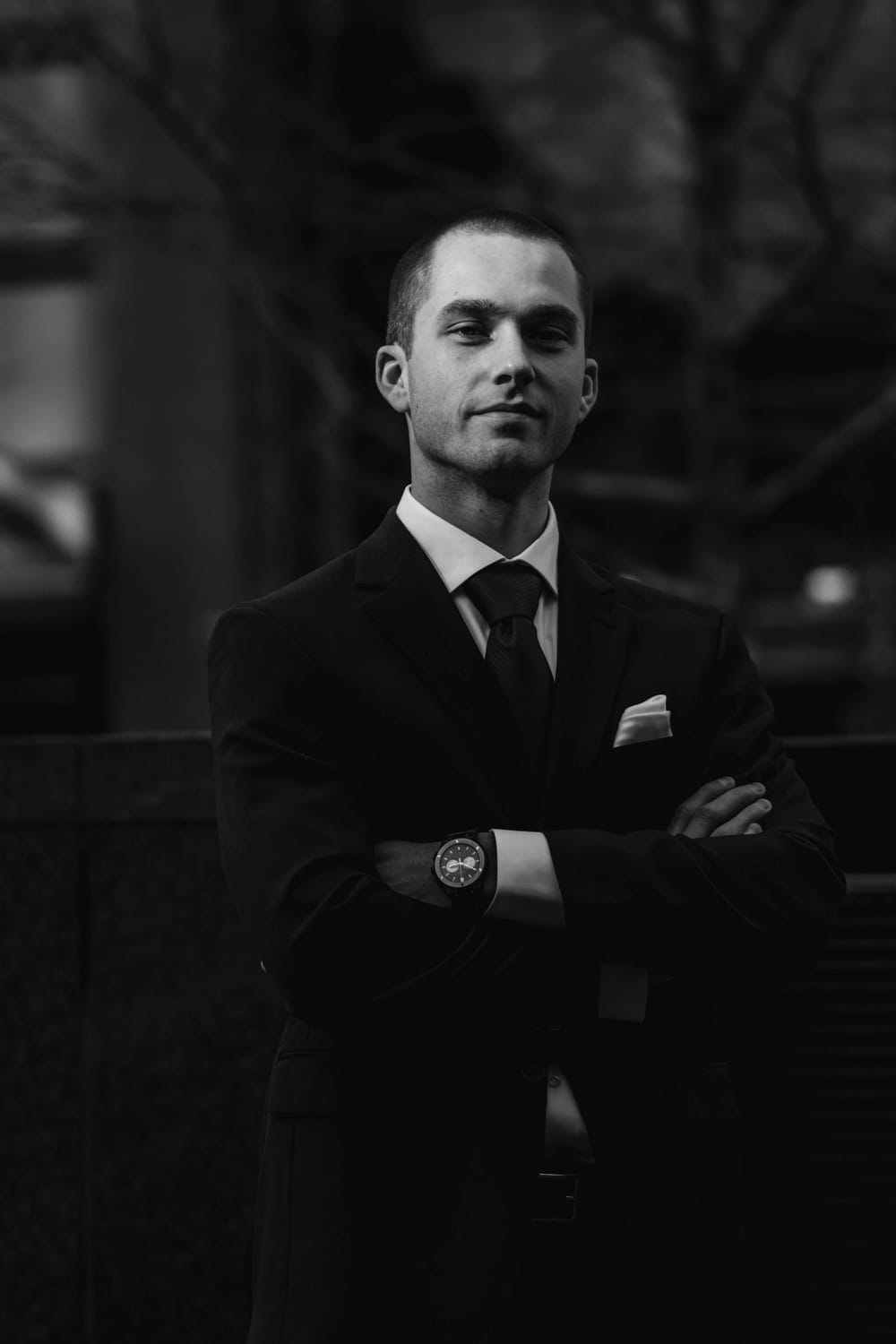 A man in a dark suit, arms crossed, low light